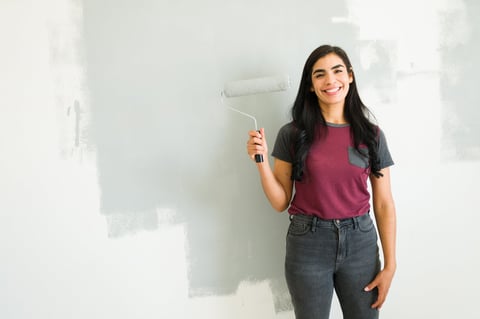 Beautiful woman painting a gray accent wall in new apartment