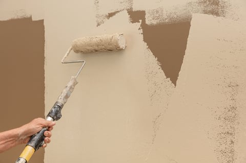 Man holding a paint roller on an extension pole painting a wall tan