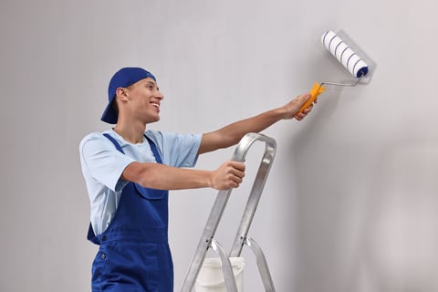 Smiling handyman painting wall with roller indoors