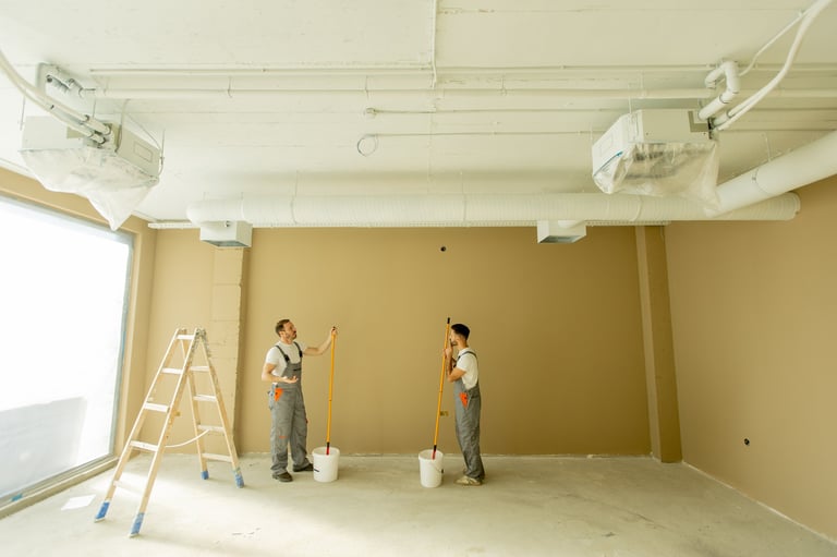 Two painters painting a wall beige in a well-lit room