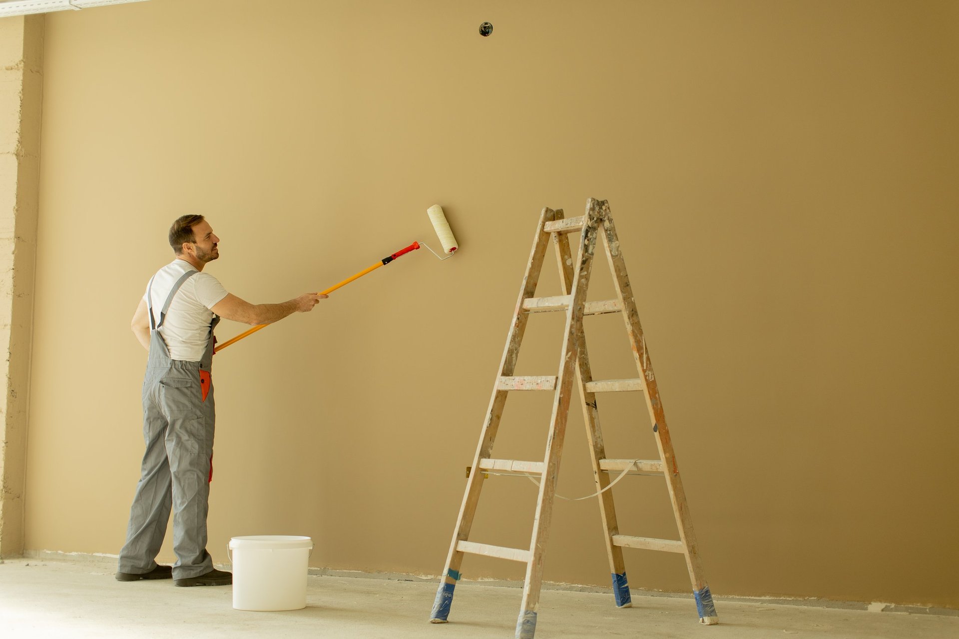 Professional painter applying light brown paint on a wall with a paint roller